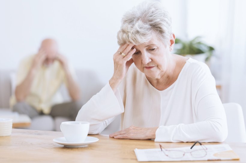 older woman sitting at table with coffee, looking distraught