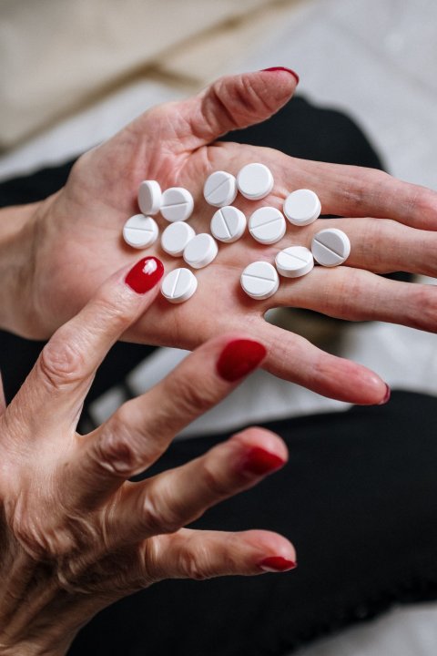 woman with red fingernails holding white pills in her hand