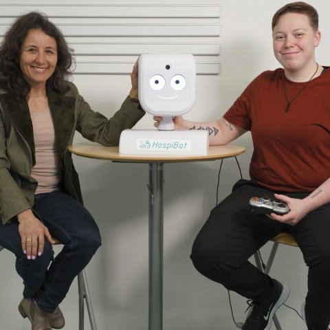 franziska uhing and miriam pfau sitting next to table with head of robot prototype on it