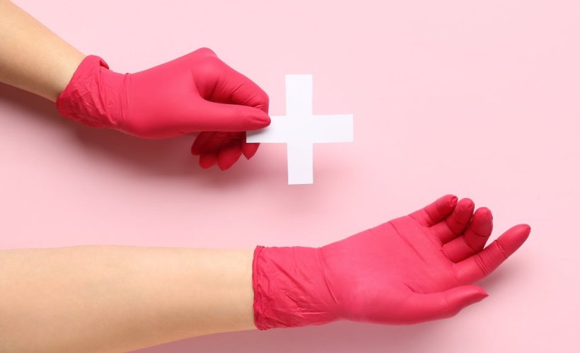 hands in pink medical gloves holding white plus symbol +