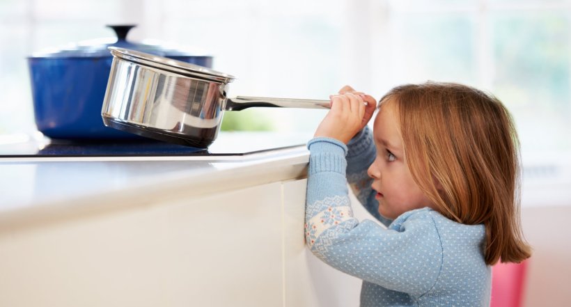 young girl reaching for hot pot on stove, risking scalding accident in the...