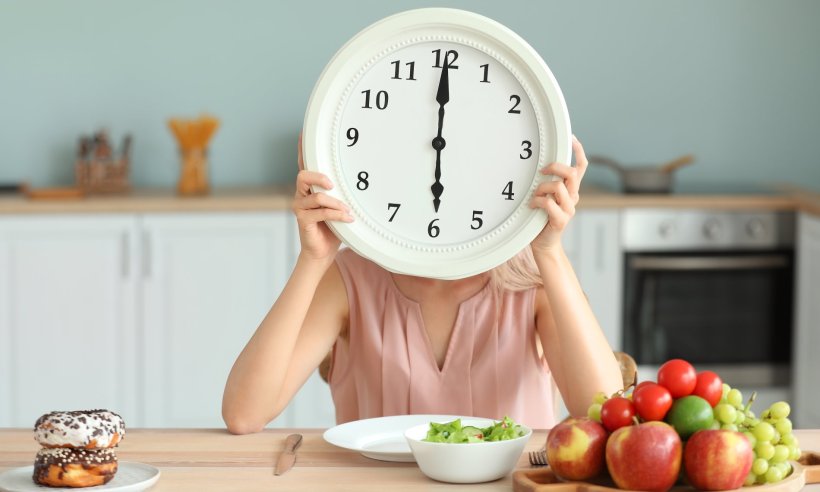 woman at dinner table holding large clock in from of her face, symbol for meal...