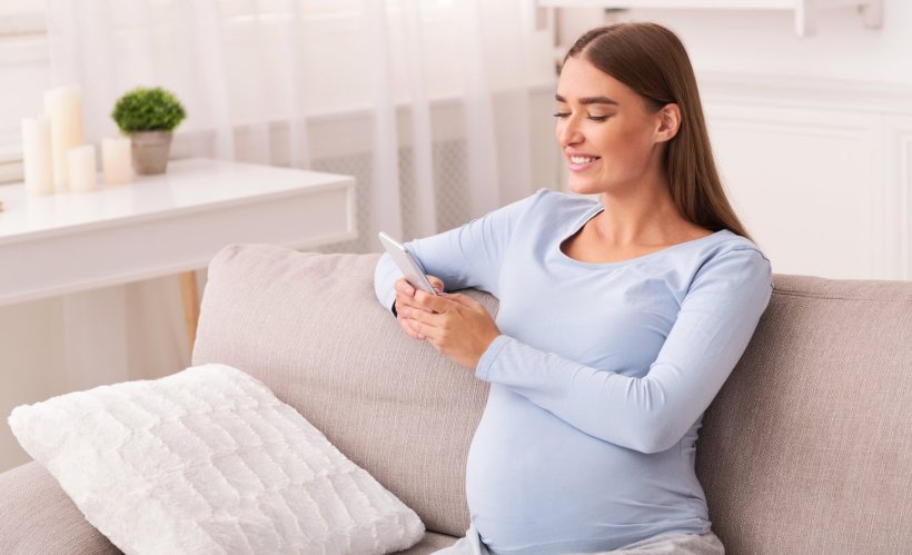 pregnant woman sitting on couch using smartphone