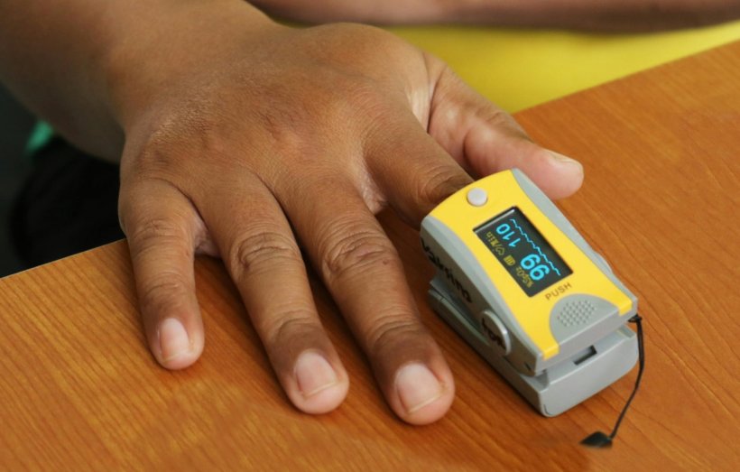 pulse oximeter on hand of person with darks skin on wooden table