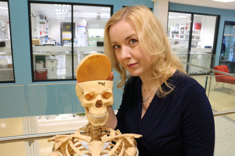 kirsi rautajoki standing next to model of childrens skeleton, with opened skull...