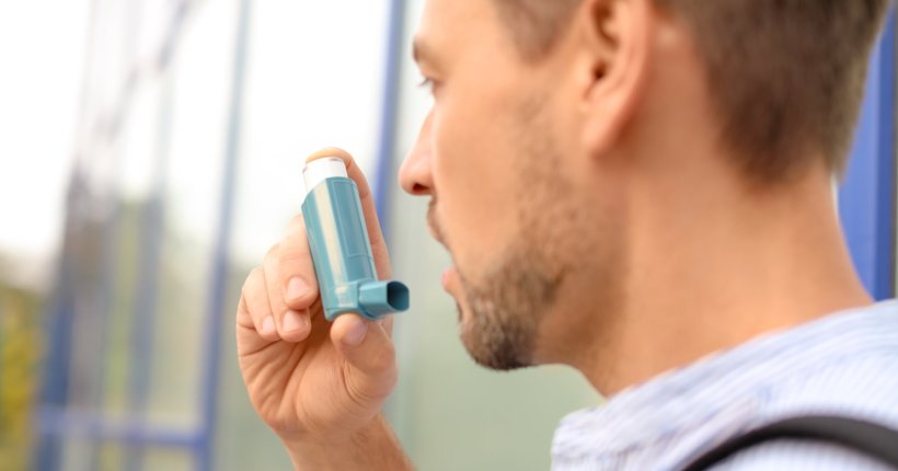 A man is using an athma inhaler outdoors