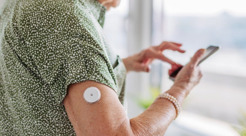 Eine ältere Frau trägt einen Sensor zur Glukosemessung bei Diabetes am Arm....