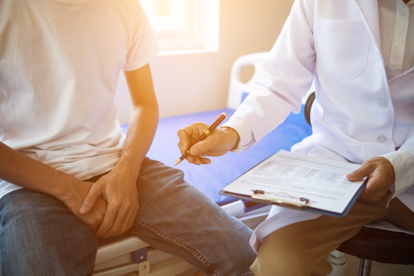 A man in a white shirt is sitting next to a doctor holding a diagnostic...