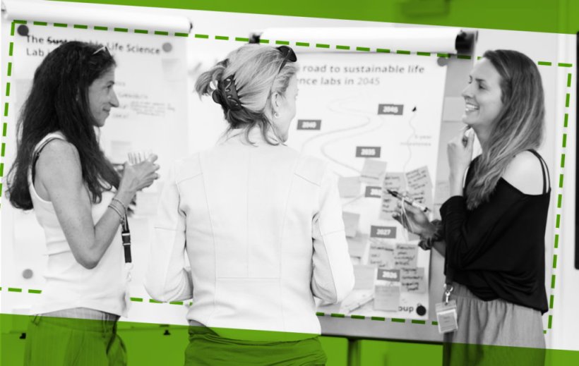 A black-and-white image of three women standing in front of a whiteboard,...