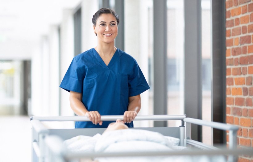 A female medical professional pushing a hospital bed across a bright hospital...