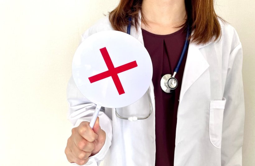 A female doctor holding a round sign with a red X on it