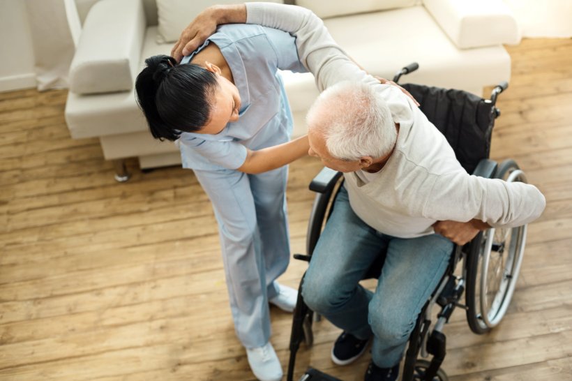 Eine junge Pflegerin hilft einem älteren Mann im Rollstuhl