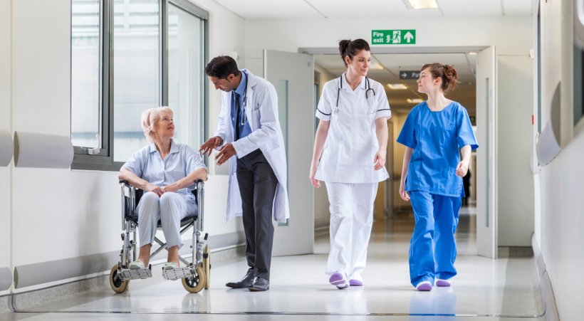 Doctors, a nurse and a senior female patient in a wheelchair standing in a...