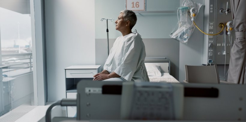 A sad woman is sitting on a hospital bed, looking out of the window