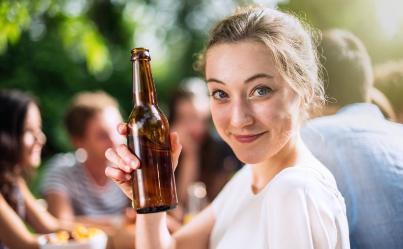 A young woman holding a bottle of beer and doing the cheers gesture