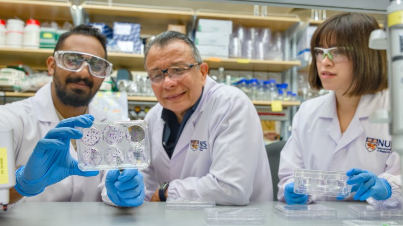 Three scientists in white lab coats sitting at a table in a laboatory...