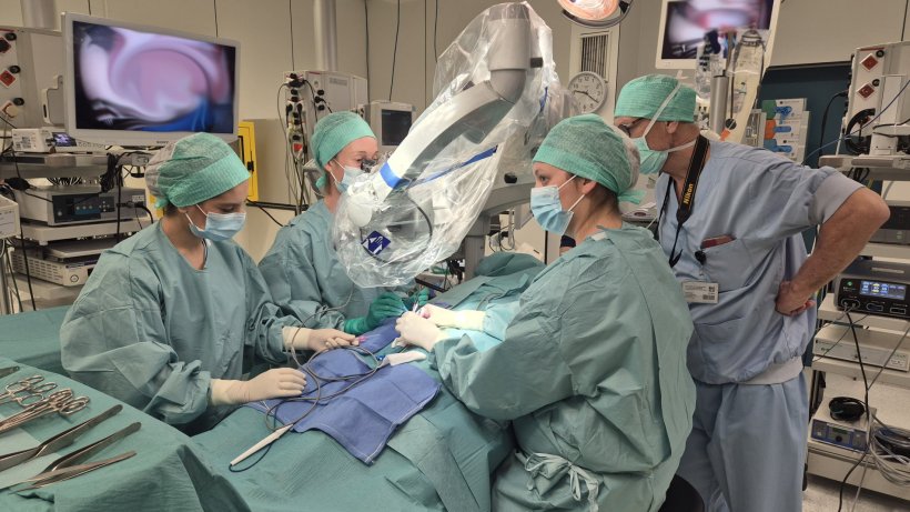 A team of surgeons performing an operation on a person covered by green...