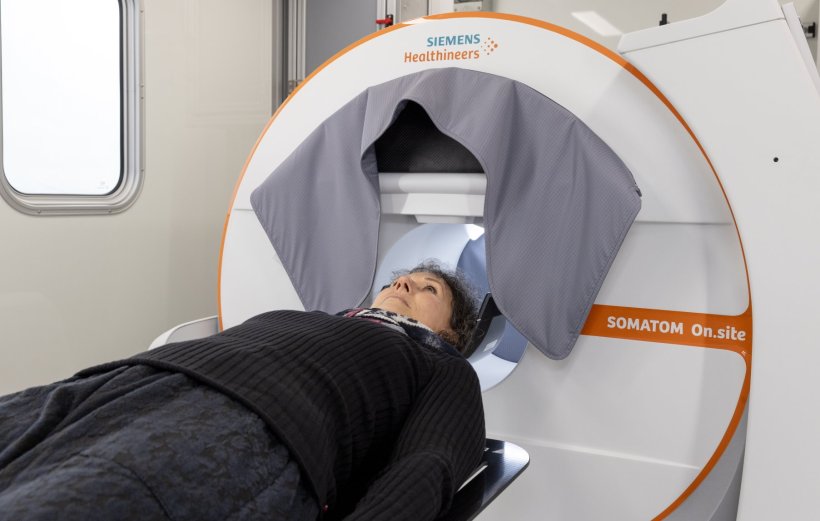 A woman is lying on a stretcher, with her head positioned in a mobile CT scanner