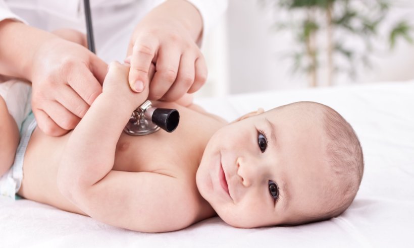 A baby smiling into the camera, a doctor holds a stethoscope to his heart