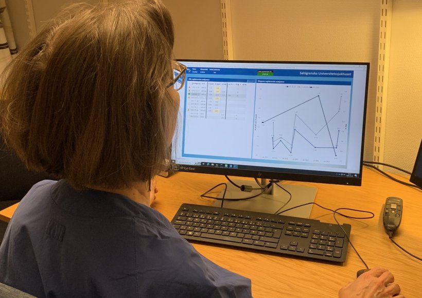 View over the shoulder of a woman looking at a computer monitor with numbers...