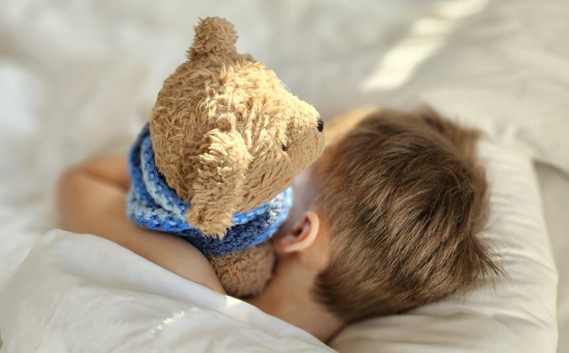 Ein kleiner Junge schläft im Bett und kuschelt mit seinem Teddybär