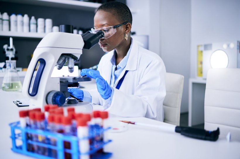 Eine junge Wissenschaftlerin im weißen Laborkittel blickt in ein Mikroskop....