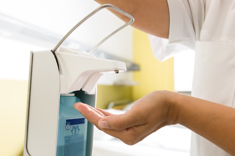 A medical professional is using a pump dispenser for hand disinfection,...