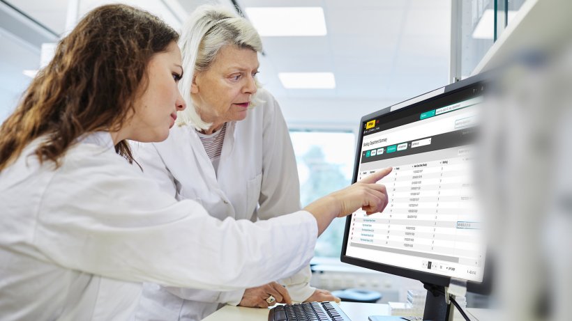 Zwei Frauen in weißen Laborkitteln schauen auf einen Monitor, auf dem eine...