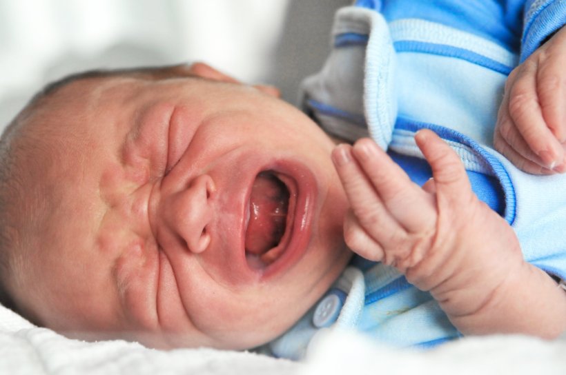 Ein weinendes Neugeborenes Baby liegt auf einem Bett
