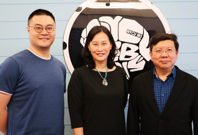 Two men and a woman are standing in front of a research lab logo shaped like a...