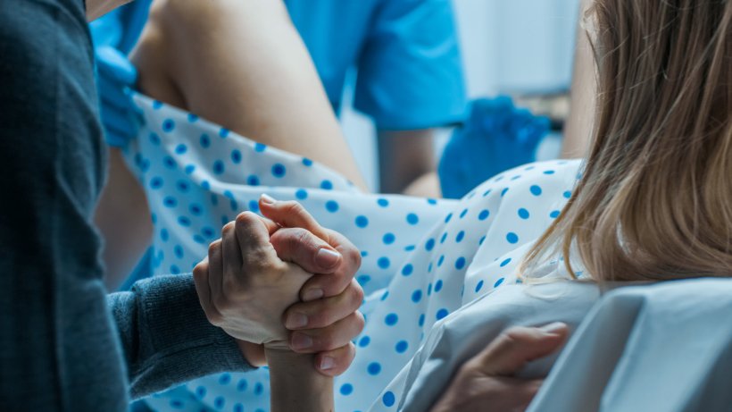 Woman giving birth at a hospital. Her husband is holding her hand, while a...