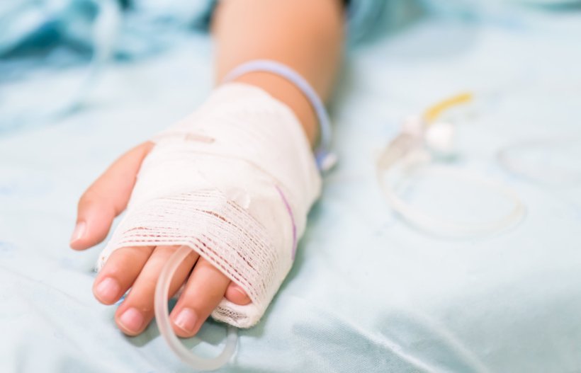 Closeup photo on the bandaged hand of a child on a hospital bed, with a plastic...