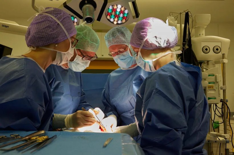 Vier Chirurgen mit Masken und Schutzhauben stehen im OP um einen Patienten, der...
