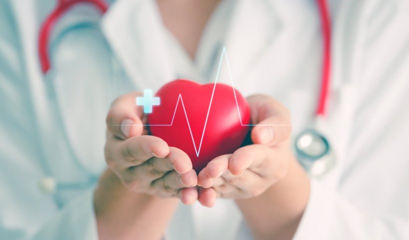 Ein rotes Herz mit darüberliegender EKG-Kurve wird von einer Medizinierin im...