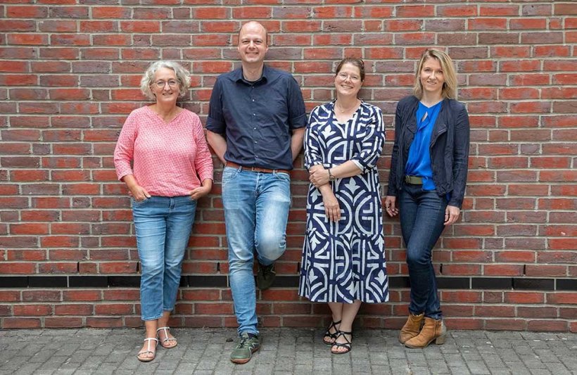 Vier Personen stehen nebeneinander an eine Backsteinmauer gelehnt