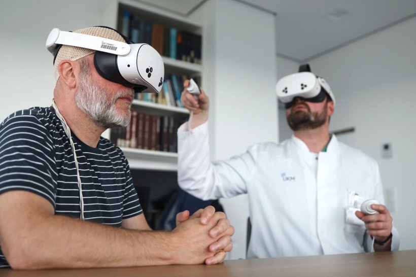 Zwei Männer mit VR-Brillen sitzen gemeinsam an einem Holztisch. Der Mann im...