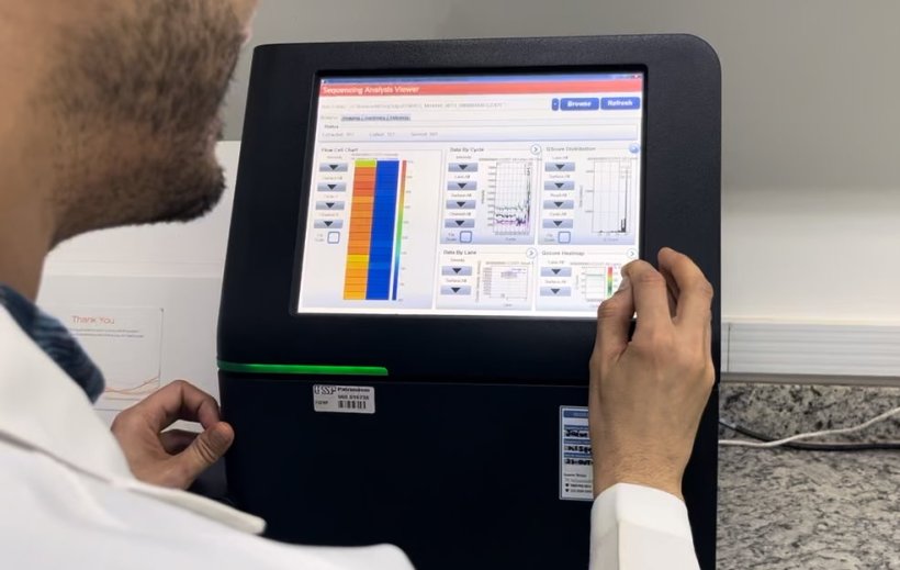 A man in a white lab coat operating a black electronic device with a...
