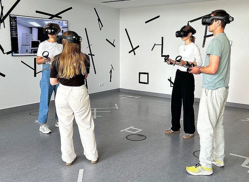 Vier Personen mit VR-Headsets und -controllern stehen in einem Raum