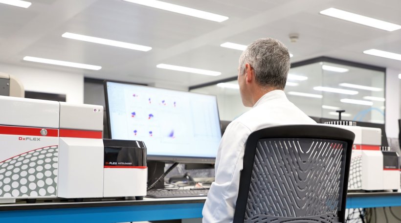 A laboratory professional sitting at a desk, looking at a computer screen