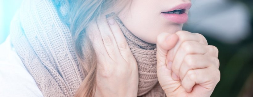 Closeup photo of a young woman coughing. She holds her balld-up right hand in...