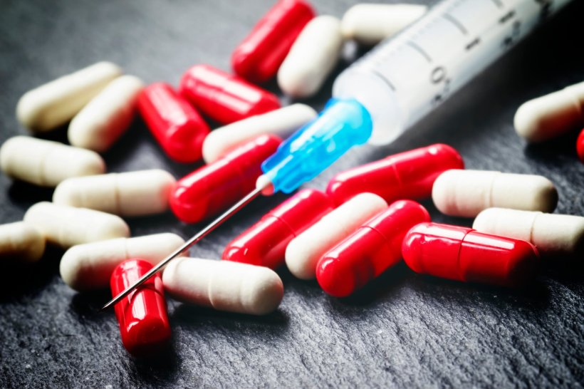 A small syringe for medical injections is placed on top of an assortment of red...