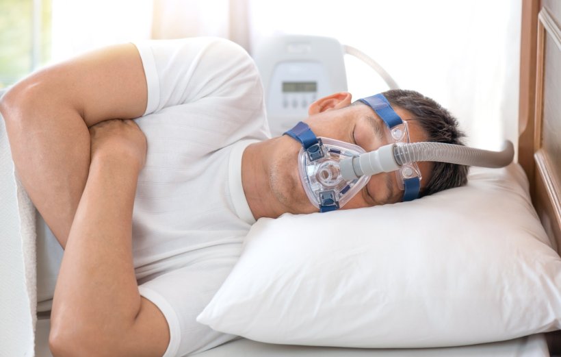 A man sleeping in a hospital bed wearing a CPAP mask for treatment of sleep...