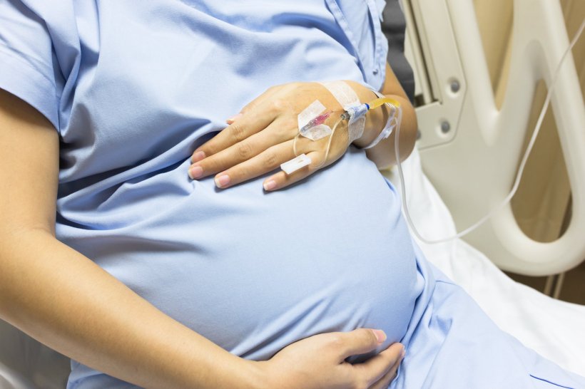 A pregnant woman is lying in a hospital bed with an IV drip attached to her...