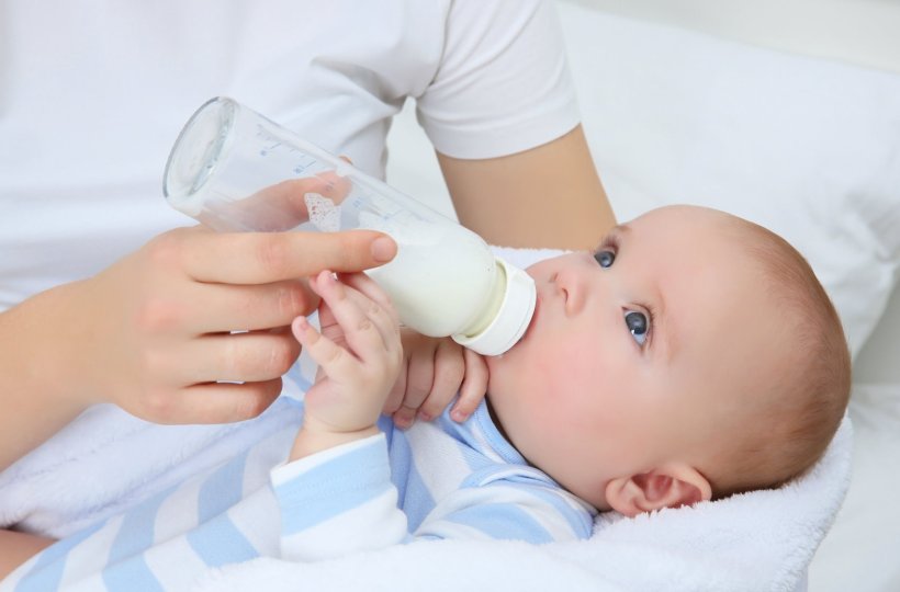 A newborn baby is feeding from a milk bottle held by their mother