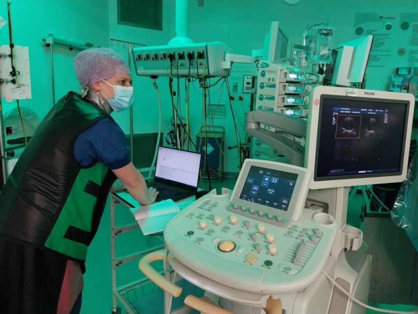 A woman wearing medical protective equipment is operating a laptop next to an...