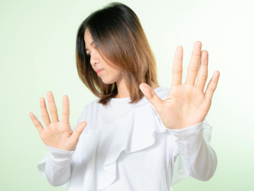 Eine junge Frau hält beide Handflächen hoch, in einer ablehnenden Geste. Ihr...