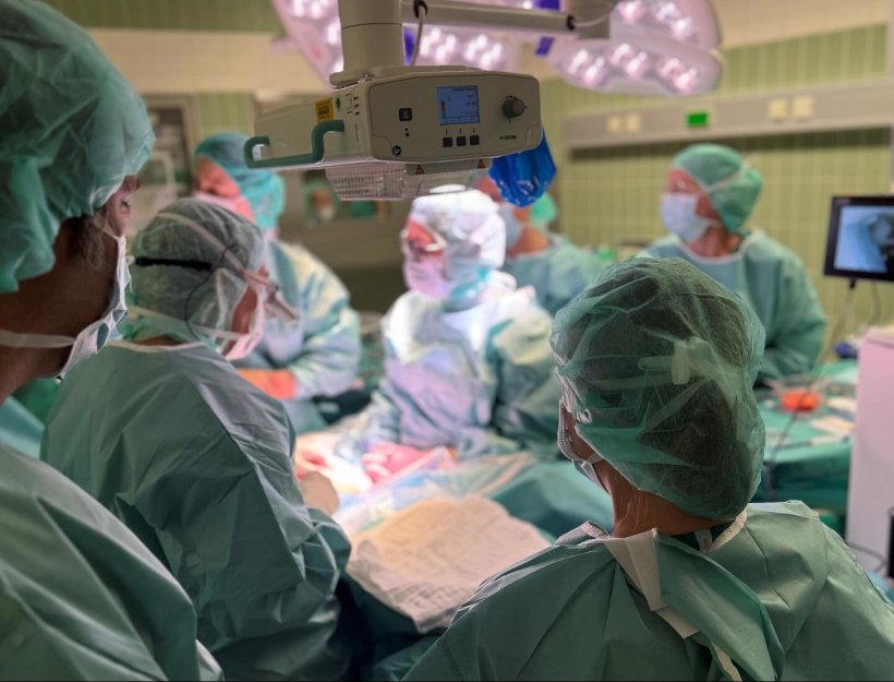 Ein Team von Chirurgen in grünen OP-Kitteln steht im Kreißsaal um eine...