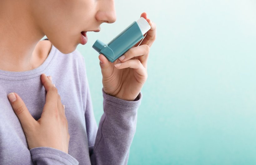 Eine junge Frau hält in der linken Hand einen Inhalator für ihr Asthma. Der...
