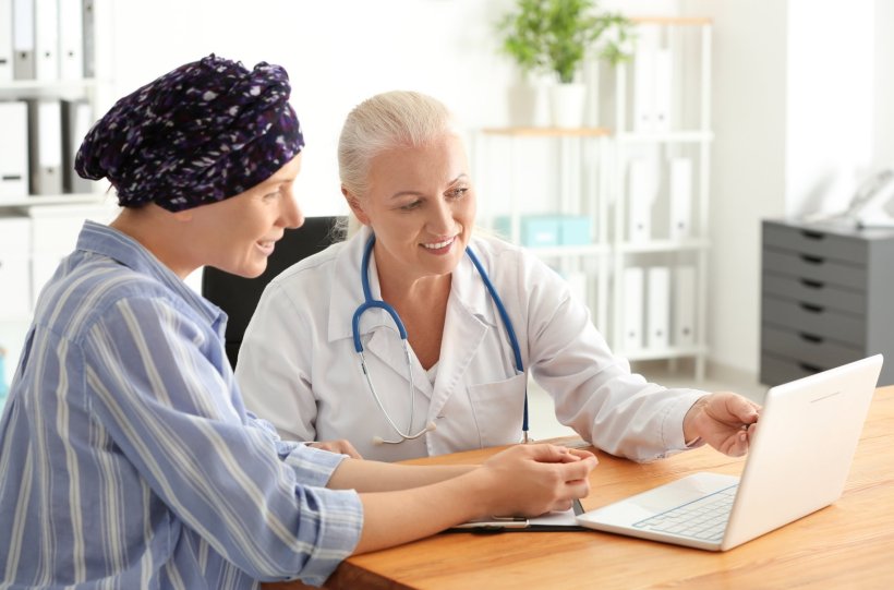 A female cancer patient wearing a headscarf consulting with her doctor. Both...