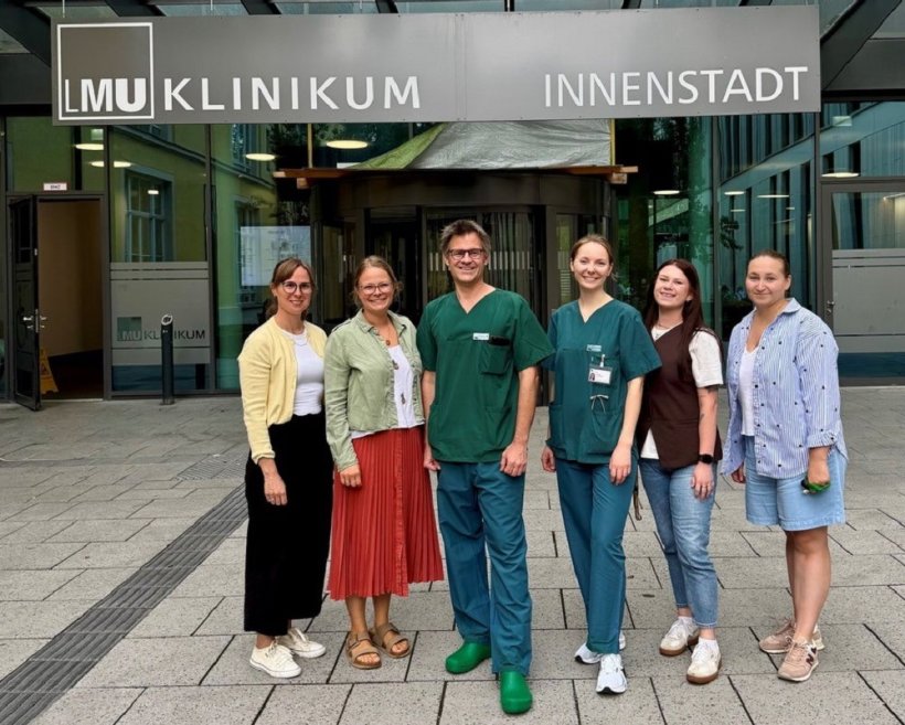 Sechs Personen stehen für ein Gruppenfoto nebeneinander vor dem Eingang des...